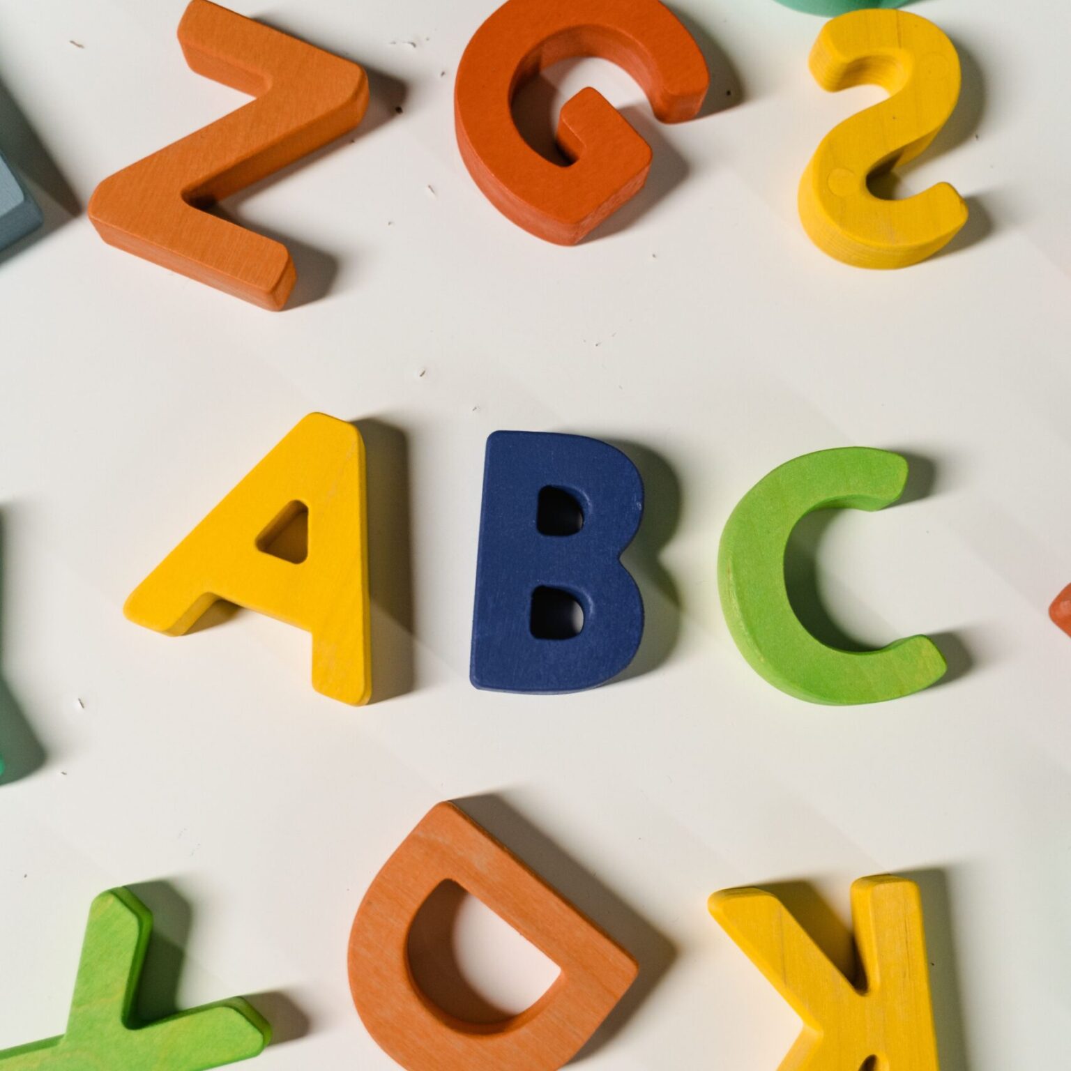 Bright, colorful wooden letters scattered on a white surface forming the alphabet.